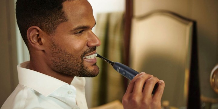 A man using the Philips Sonicare 9900 Prestige Rechargeable Electric Toothbrush and smiling.